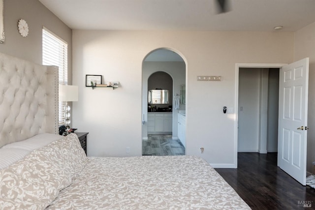 bedroom with wood finished floors, arched walkways, baseboards, and ensuite bathroom