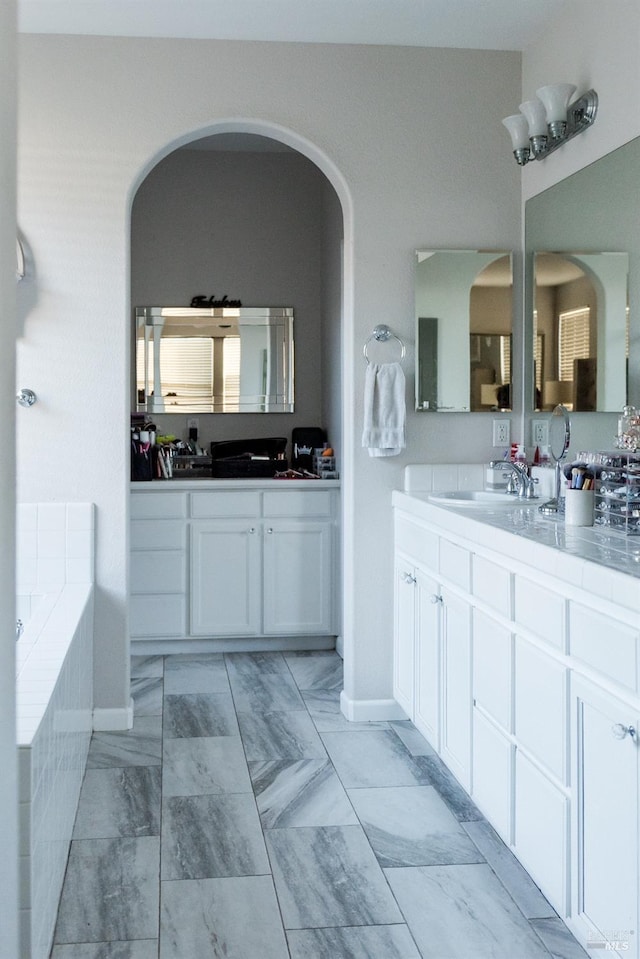 full bath with marble finish floors, a bath, and two vanities