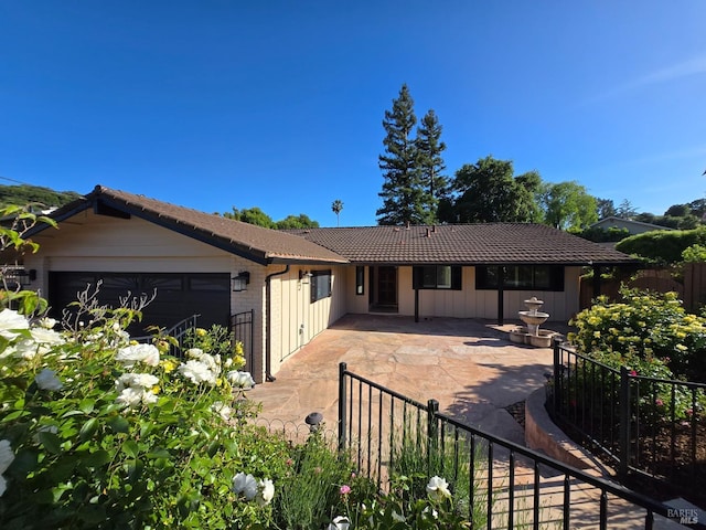view of front facade featuring fence, a garage, a tiled roof, a patio, and board and batten siding