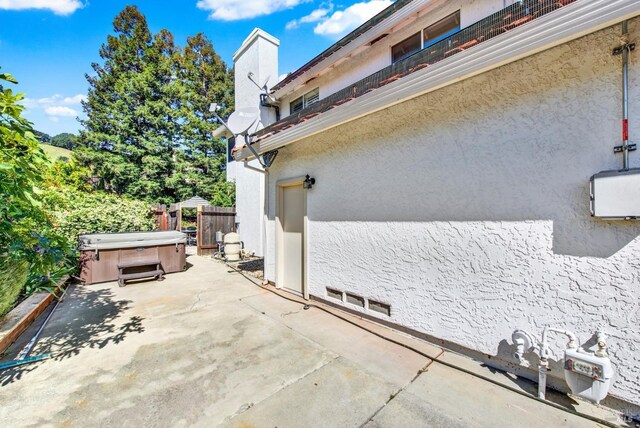 view of side of home featuring a hot tub, a patio, stucco siding, and fence