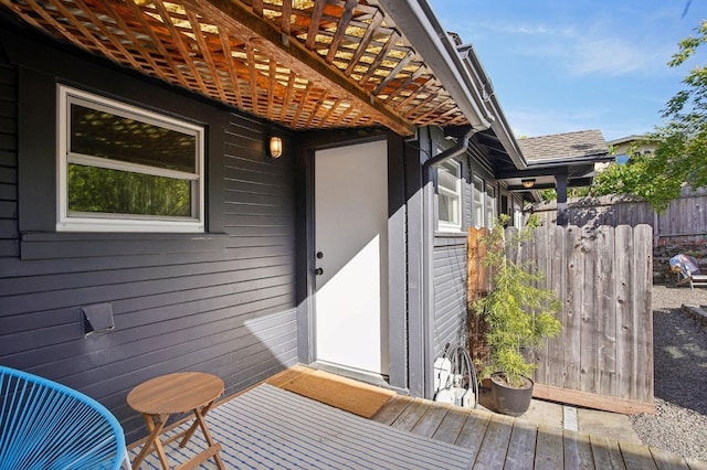 view of exterior entry with fence and roof with shingles