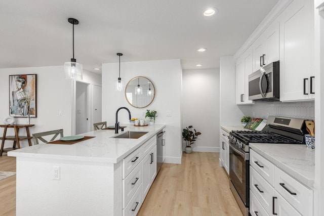 kitchen with appliances with stainless steel finishes, a sink, a peninsula, light wood finished floors, and white cabinetry