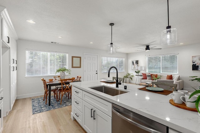 kitchen with a sink, stainless steel dishwasher, light wood-style floors, pendant lighting, and a textured ceiling