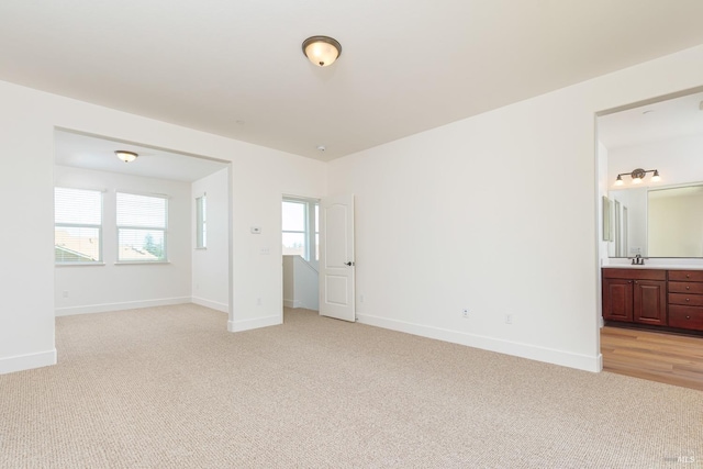 unfurnished bedroom featuring light carpet, baseboards, ensuite bath, and a sink