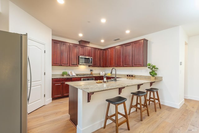 kitchen with stainless steel appliances, a sink, a peninsula, light wood-style floors, and recessed lighting
