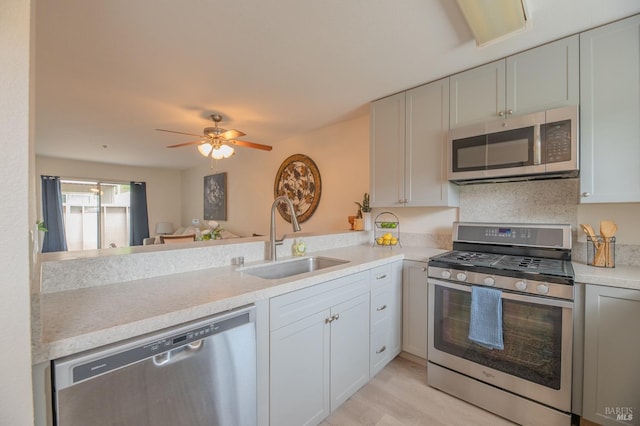 kitchen with stainless steel appliances, a sink, light countertops, a ceiling fan, and light wood-style flooring