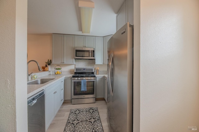 kitchen with appliances with stainless steel finishes, a sink, light countertops, and light wood-type flooring