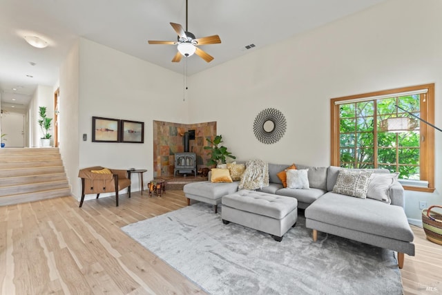 living room featuring a ceiling fan, light wood-type flooring, a wood stove, baseboards, and stairs