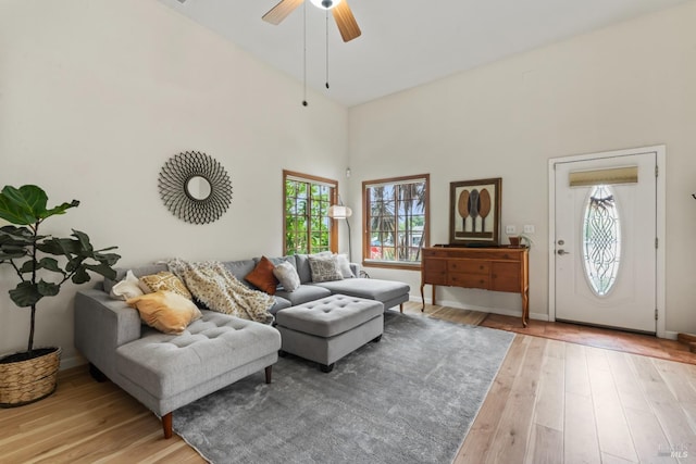 living room with light wood-type flooring, a ceiling fan, baseboards, and a high ceiling