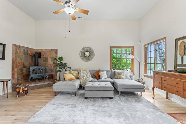 living area featuring wood finished floors, ceiling fan, a wood stove, a high ceiling, and baseboards