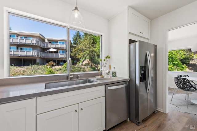 kitchen with stainless steel appliances, a sink, wood finished floors, white cabinetry, and decorative light fixtures