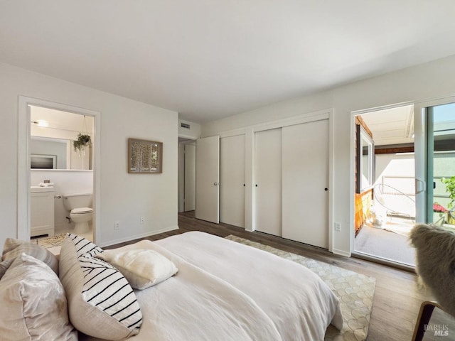 bedroom featuring multiple closets, wood finished floors, ensuite bath, and baseboards