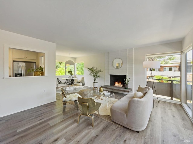 living room featuring wood finished floors, plenty of natural light, a brick fireplace, and baseboards