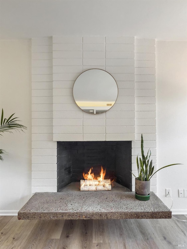 detailed view of a fireplace, wood finished floors, and baseboards