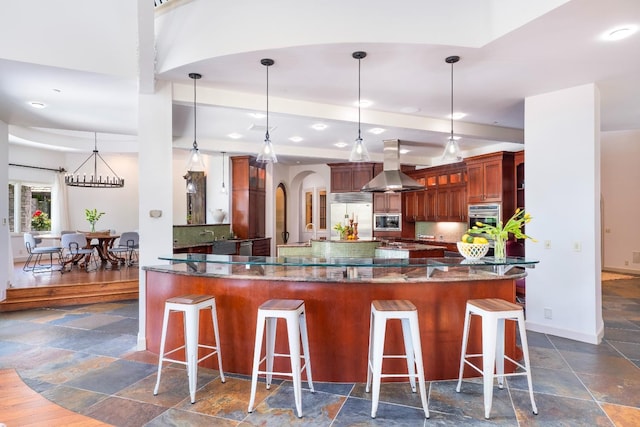 27681 Mace Blvd, Davis, CA 95618 - kitchen featuring island exhaust hood, built in appliances, stone tile flooring, dark stone counters, and a kitchen bar