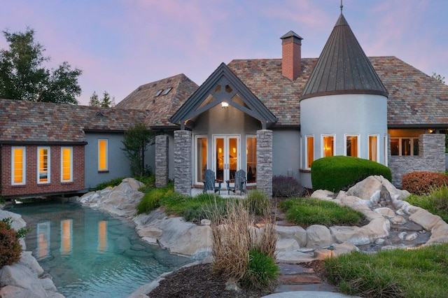 27681 Mace Blvd, Davis, CA 95618 - back of house at dusk featuring french doors, stone siding, stucco siding, a chimney, and a high end roof