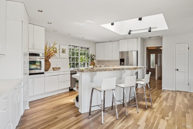 kitchen featuring stainless steel appliances, a kitchen breakfast bar, tasteful backsplash, a center island, and light wood-style flooring