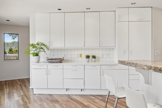 kitchen featuring decorative backsplash, light wood-type flooring, baseboards, white cabinets, and recessed lighting