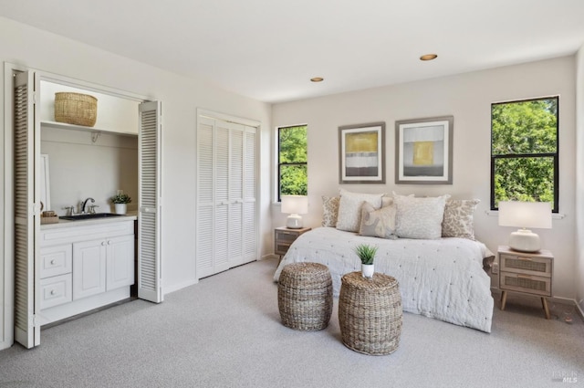 bedroom with light colored carpet, a sink, baseboards, and two closets