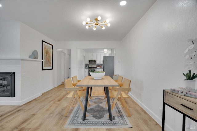 dining area featuring baseboards, light wood finished floors, a chandelier, a glass covered fireplace, and recessed lighting