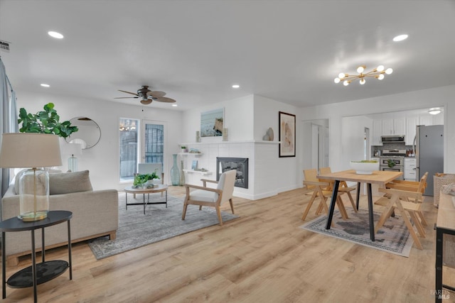 living room featuring light wood-type flooring, a fireplace, a chandelier, ceiling fan, and recessed lighting