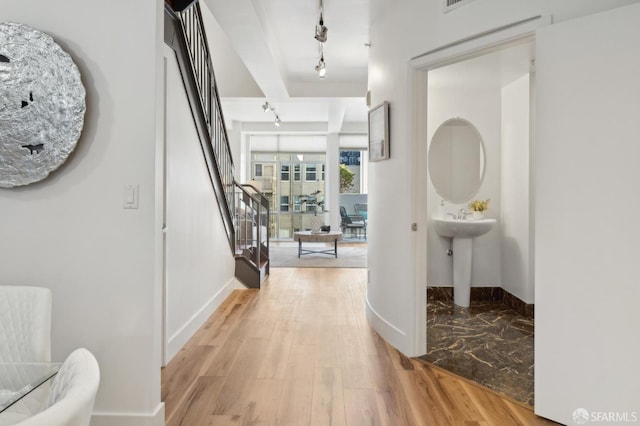 hallway with track lighting, light wood-style flooring, stairs, and baseboards