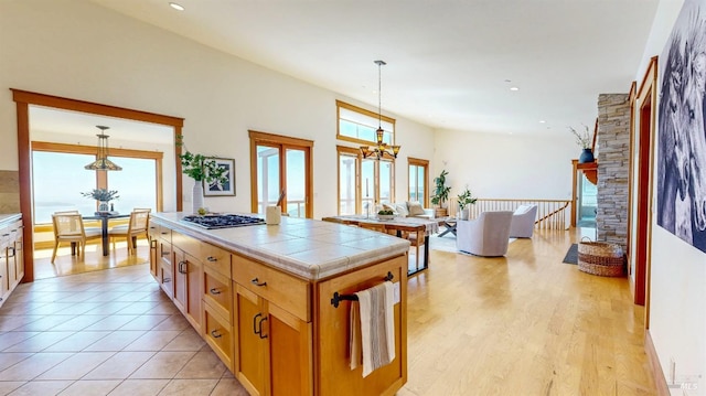 kitchen with tile counters, a kitchen island, recessed lighting, decorative light fixtures, and light wood finished floors