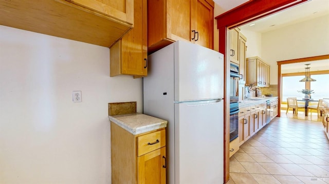 kitchen with freestanding refrigerator, light countertops, light tile patterned floors, a sink, and pendant lighting