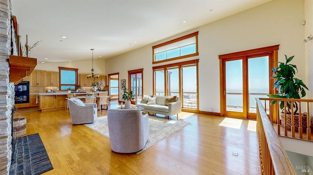 living area with light wood-type flooring, a fireplace, recessed lighting, a chandelier, and a high ceiling