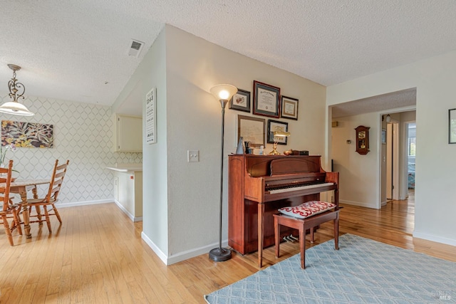 sitting room with wallpapered walls, an accent wall, light wood-type flooring, baseboards, and a textured ceiling