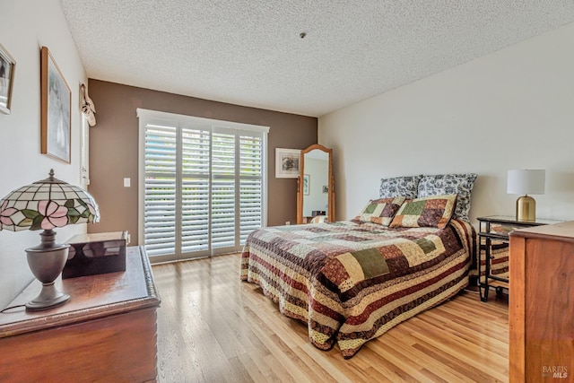 bedroom with light wood finished floors, access to exterior, and a textured ceiling