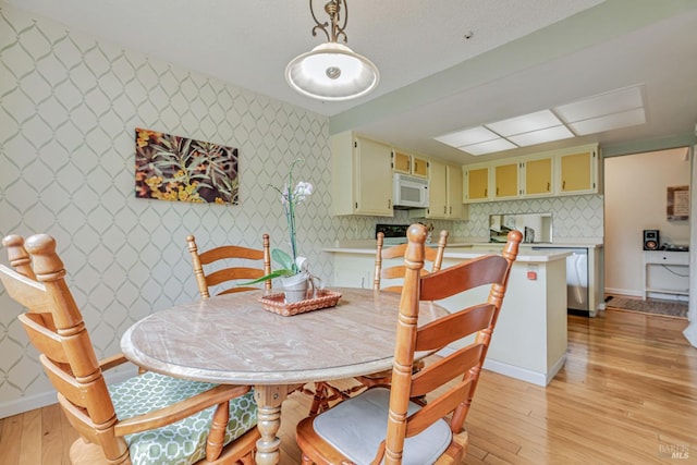 dining room featuring wallpapered walls, light wood-style floors, and baseboards