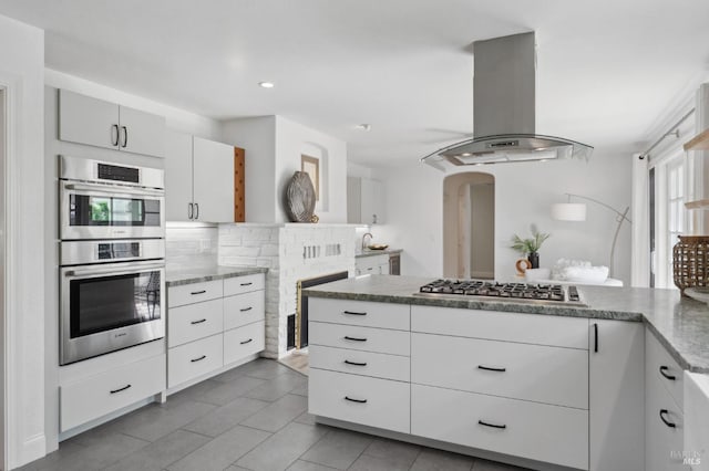 249 Los Palos St, Sonoma, CA 95476 - kitchen with stainless steel appliances, island range hood, decorative backsplash, a peninsula, and light tile patterned floors