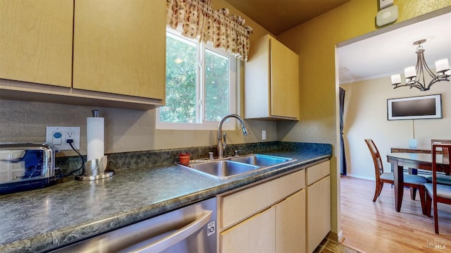 kitchen with dark countertops, stainless steel dishwasher, a sink, a chandelier, and pendant lighting