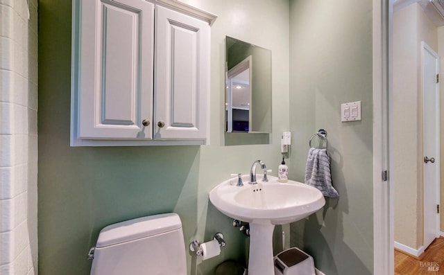 half bath with toilet, wood finished floors, and baseboards