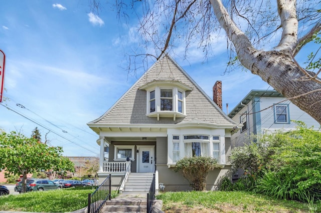 victorian house featuring a porch, stairway, and a chimney