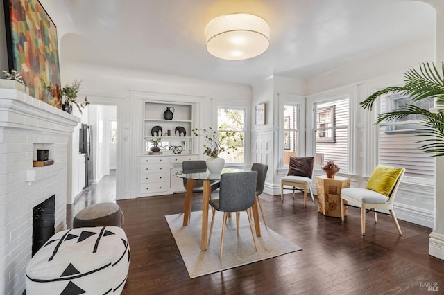 dining room with a brick fireplace, dark wood-style floors, and built in shelves
