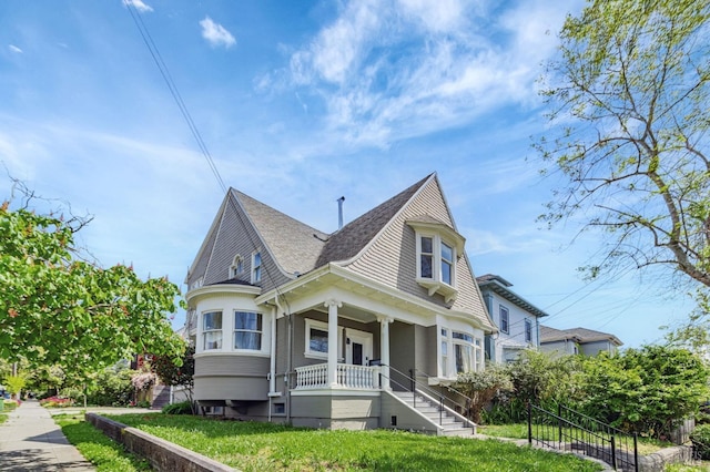 victorian home featuring covered porch, a shingled roof, and stairway