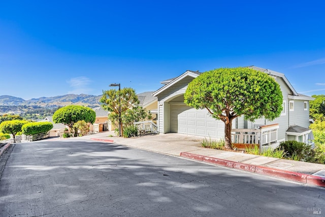 view of property hidden behind natural elements featuring concrete driveway, an attached garage, and a mountain view