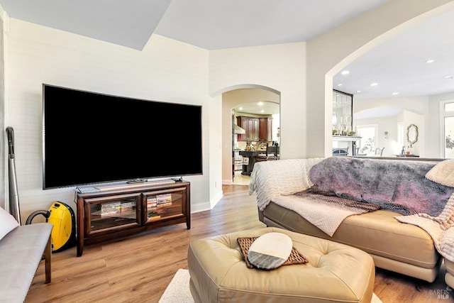living area with arched walkways, light wood finished floors, and recessed lighting
