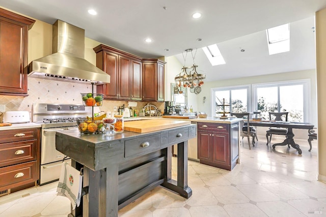 kitchen with stainless steel gas stove, wall chimney range hood, a skylight, light countertops, and recessed lighting