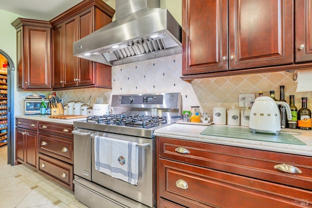 kitchen featuring stainless steel range with gas stovetop, wall chimney range hood, light countertops, and tasteful backsplash