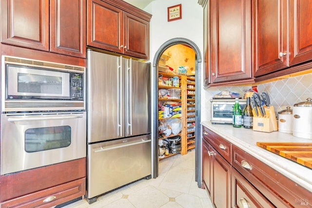 kitchen featuring stainless steel appliances, tasteful backsplash, reddish brown cabinets, light tile patterned floors, and light countertops