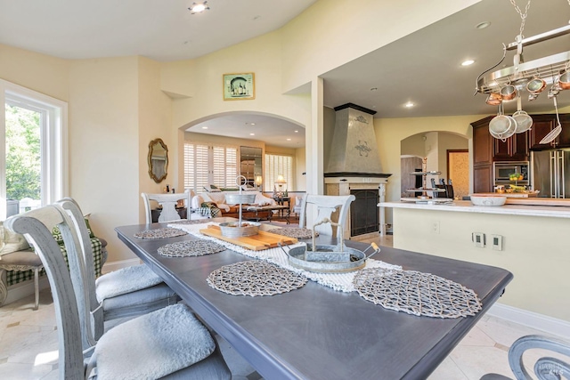 dining space featuring arched walkways, a large fireplace, baseboards, recessed lighting, and vaulted ceiling