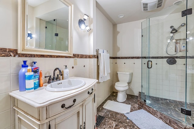 bathroom with tile walls, a shower stall, toilet, vanity, and marble finish flooring