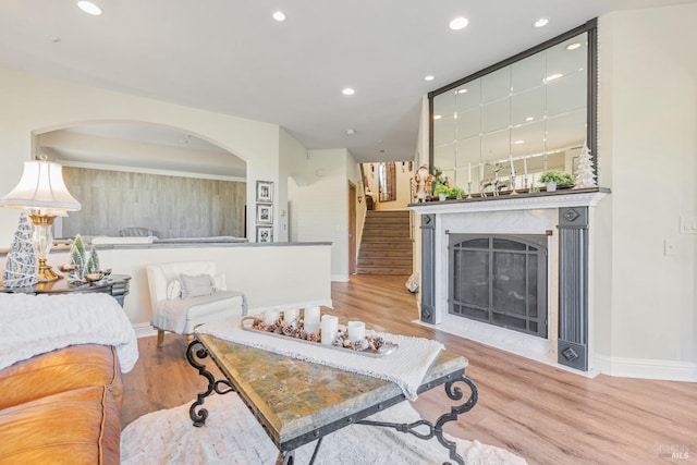 living room featuring wood finished floors, a fireplace with flush hearth, arched walkways, baseboards, and recessed lighting