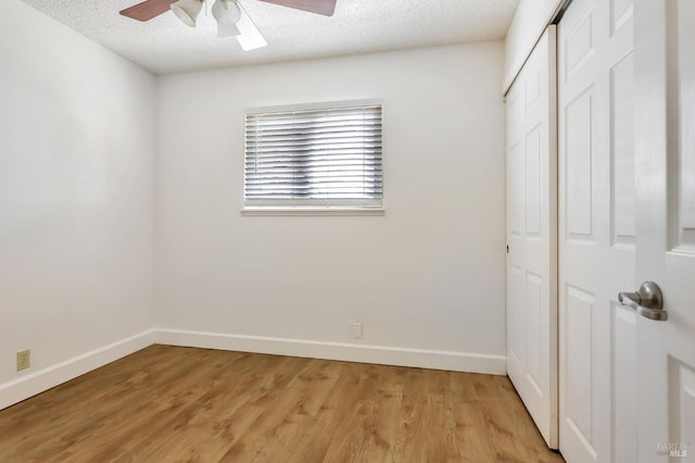 unfurnished bedroom with baseboards, light wood-type flooring, a closet, a textured ceiling, and a ceiling fan