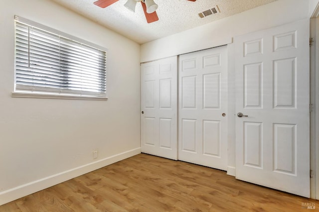 unfurnished bedroom featuring a textured ceiling, a closet, light wood-style flooring, baseboards, and a ceiling fan