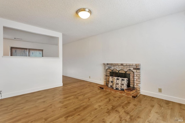 unfurnished living room with wood finished floors, a brick fireplace, baseboards, and a textured ceiling