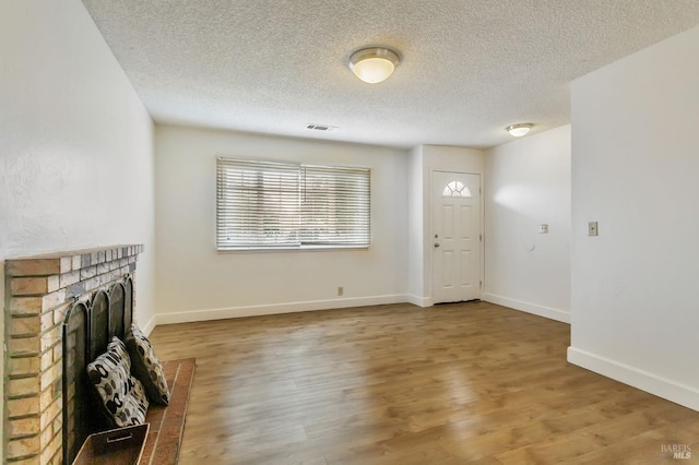 unfurnished living room with a brick fireplace, a textured ceiling, wood finished floors, and baseboards